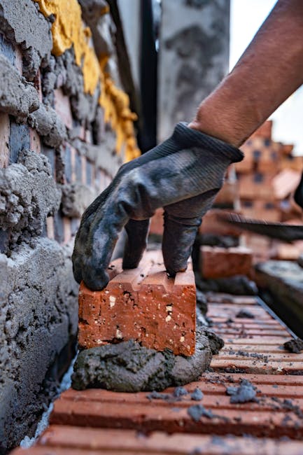 A bricklayer's gloved hand places a brick on a construction site in Vietnam.